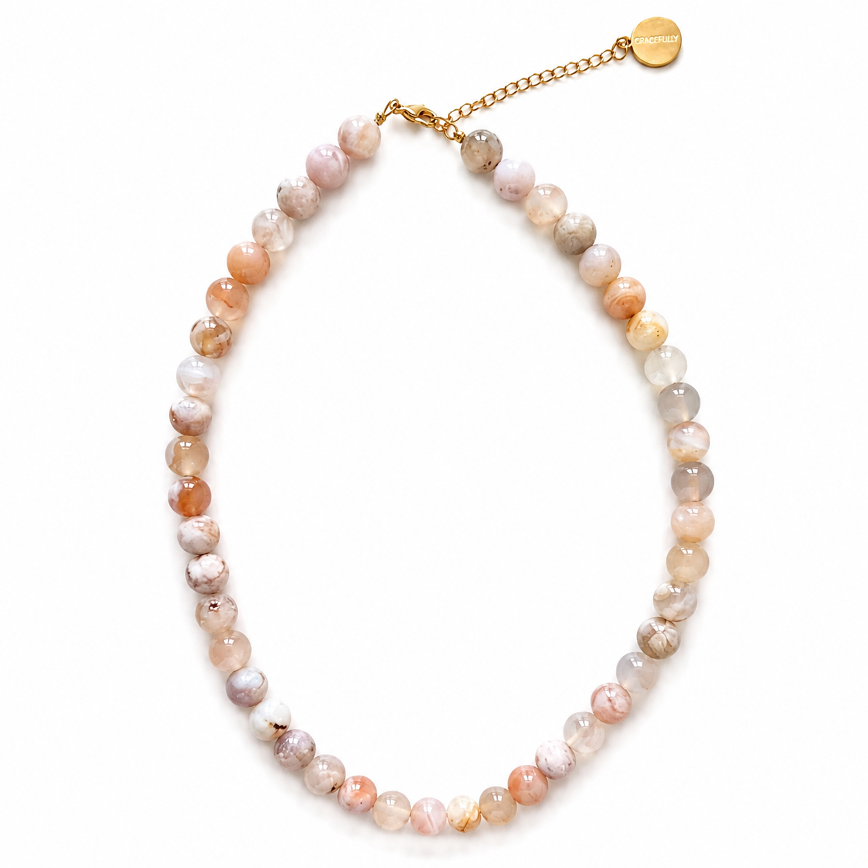 A beaded necklace made of round, polished gemstone beads in soft pastel shades of pink, peach, beige, and gray, with a gold-tone chain extender and a small round gold tag