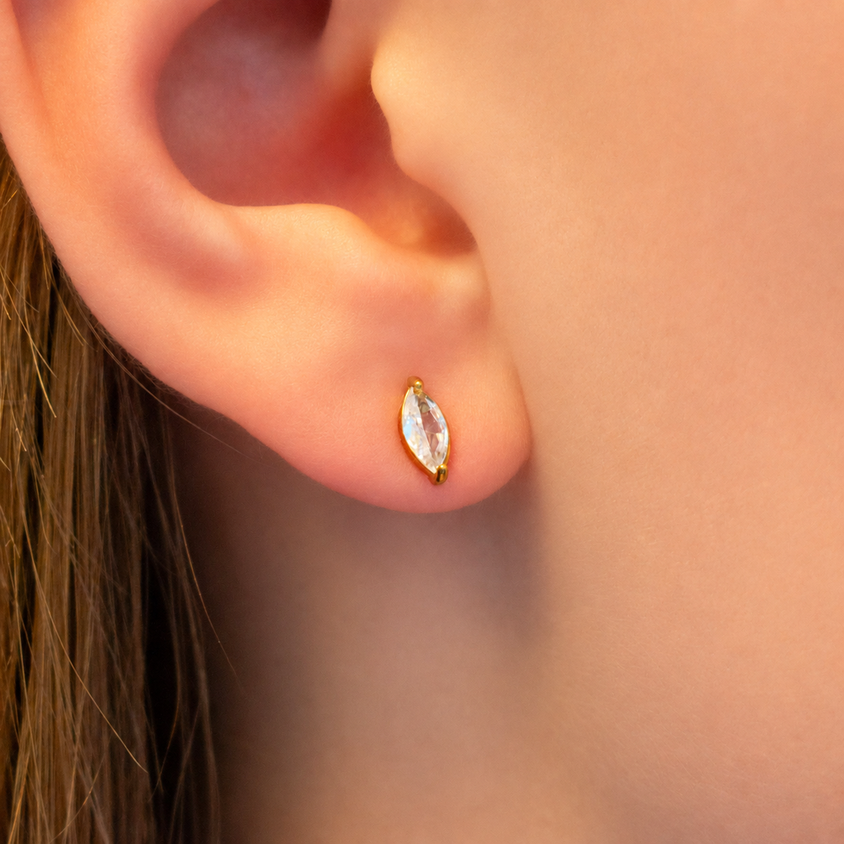 a small gold stud earring with a marquise-cut clear gemstone.