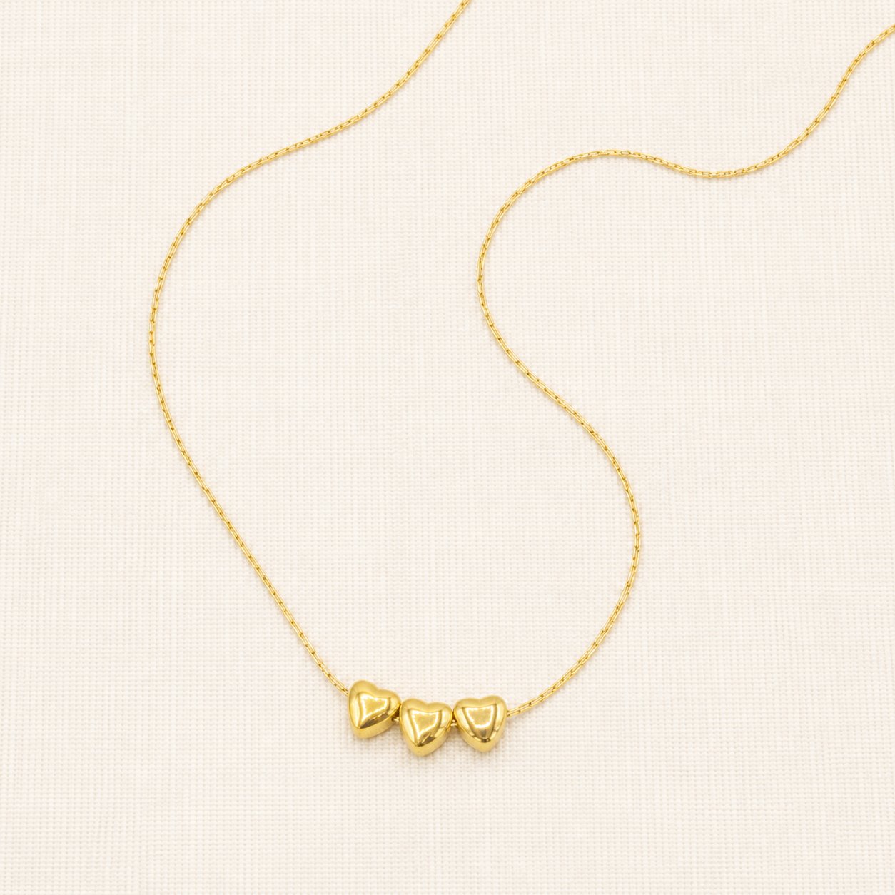 A delicate gold chain necklace featuring three small, polished gold heart charms aligned horizontally