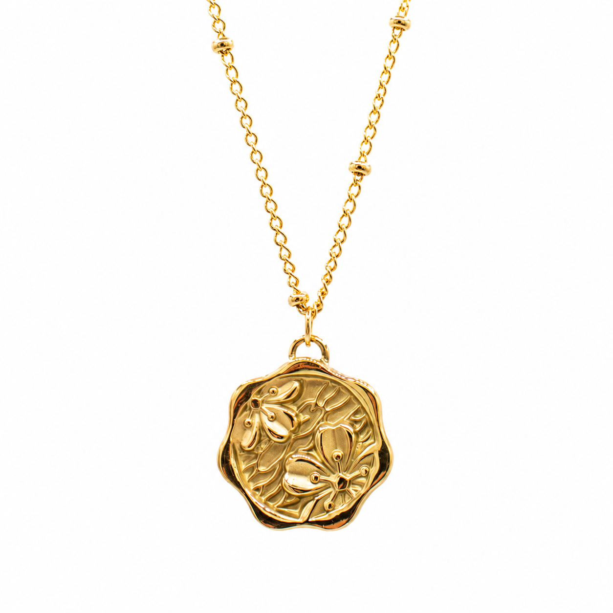 A gold necklace featuring a round, scalloped wax-seal style pendant with an embossed floral motif, suspended from a delicate gold chain