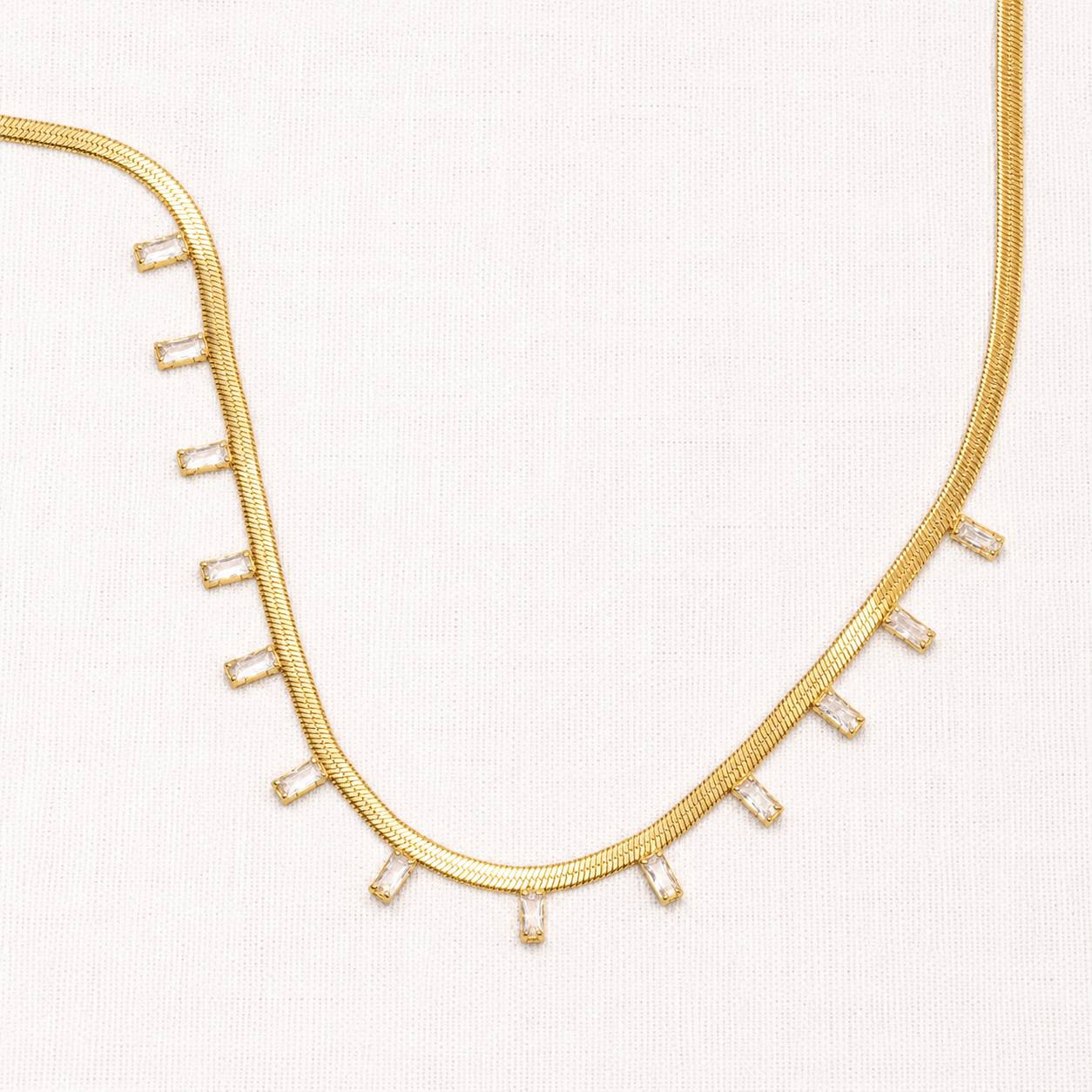 A gold snake chain necklace featuring small rectangular clear baguette and round-cut stones set along the front