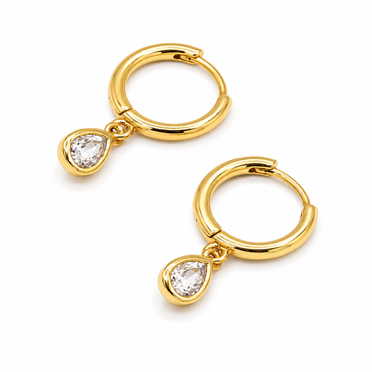 A pair of gold huggie hoop earrings with a teardrop-shaped clear gemstone dangling from the bottom