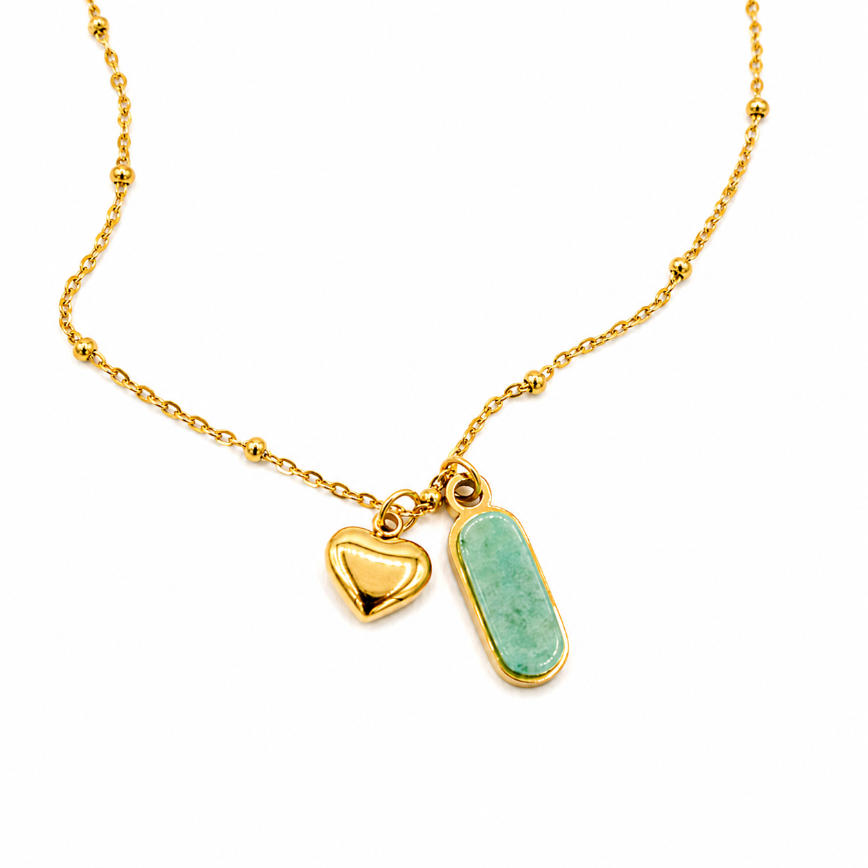 A delicate gold chain necklace featuring two charms: a small polished gold heart and a larger gold oval bezel containing a light green stone