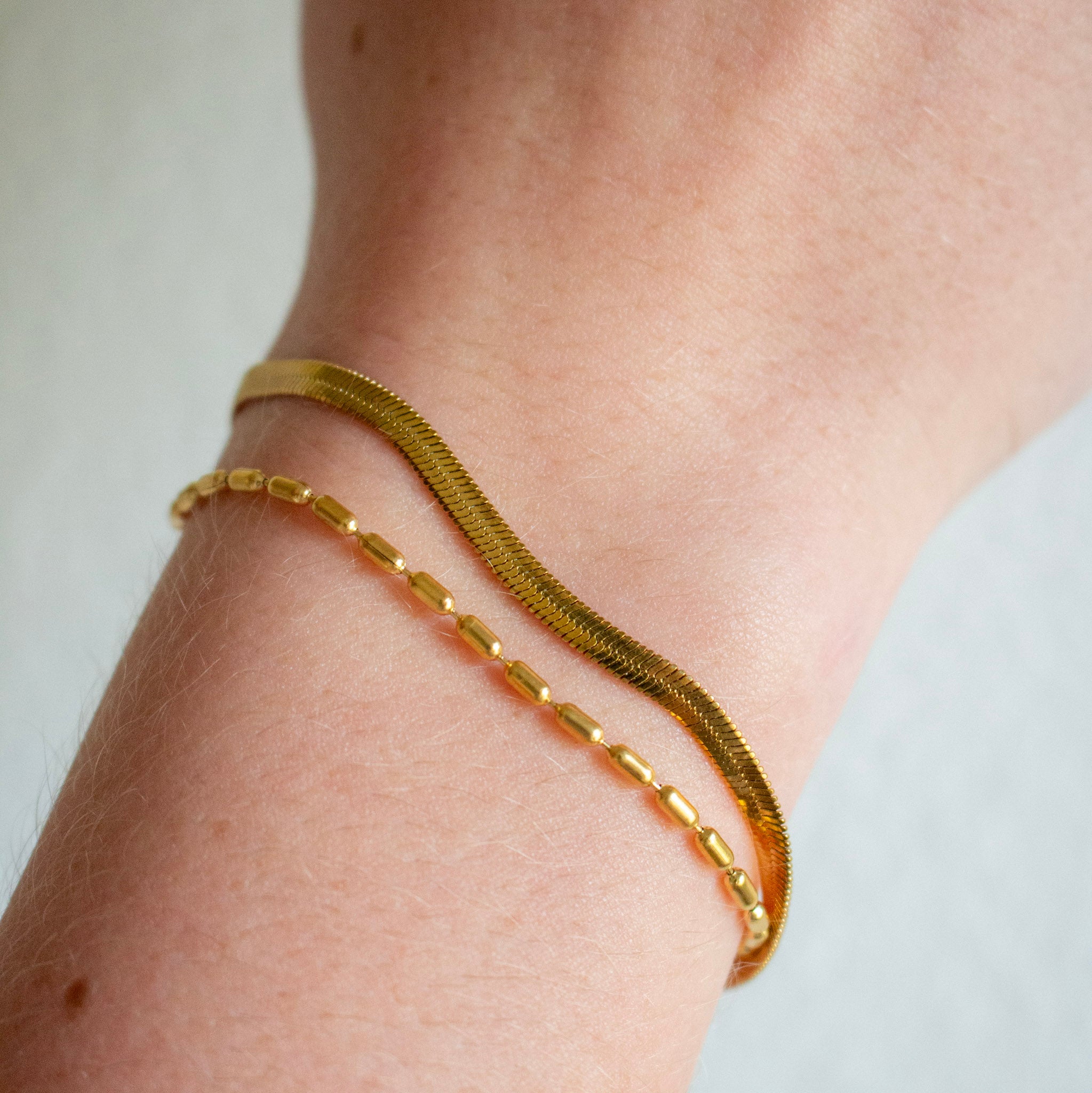 Two gold bracelets, one textured snake chain and one polished curb link chain,