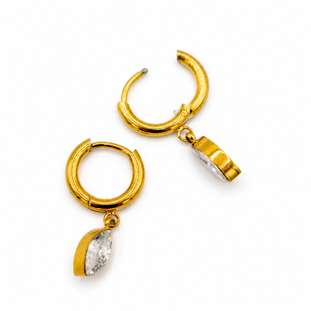 A pair of gold huggie hoop earrings with marquise-cut clear gemstones dangling from the bottom