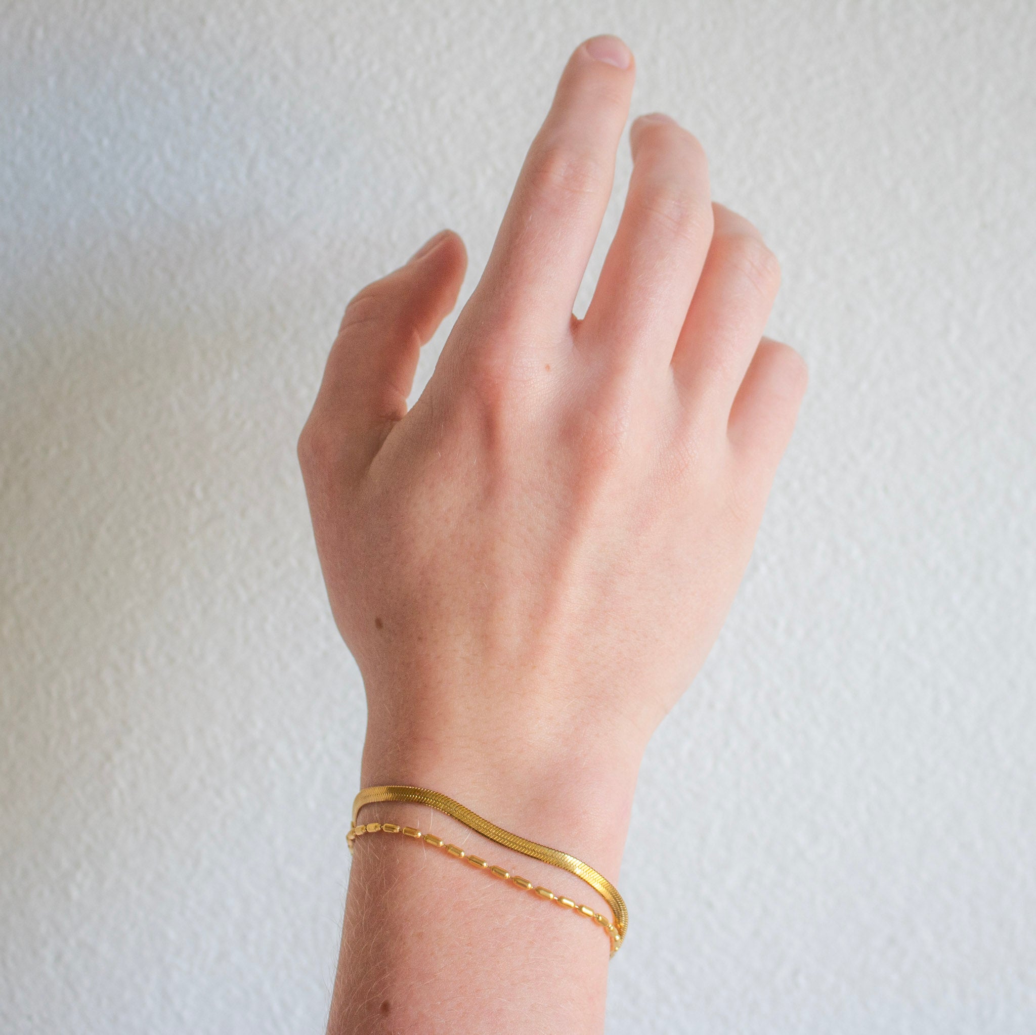 hand and wrist wearing two delicate gold bracelets