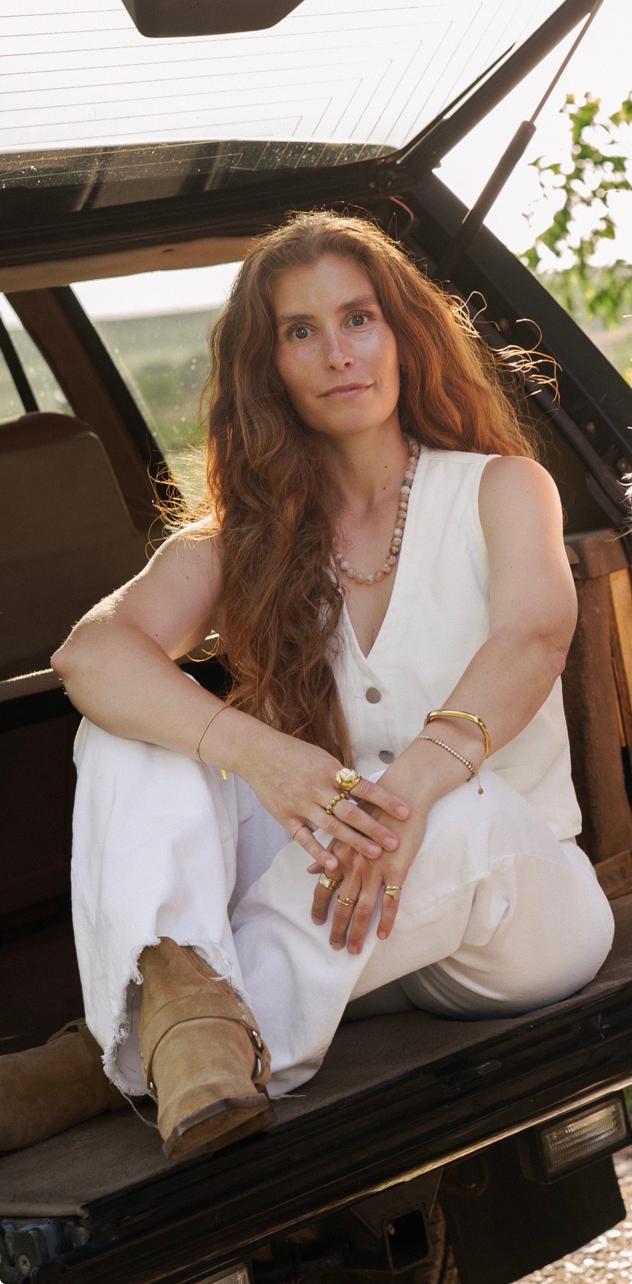 Woman sitting in the open door of a vehicle wearing a white outfit and natural stone beaded necklace