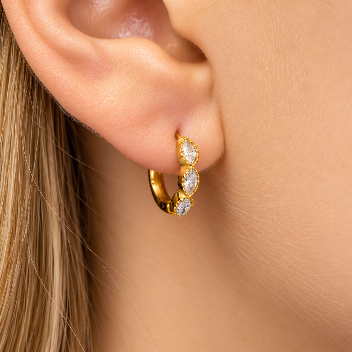 a small gold huggie hoop earring with three marquise-cut clear stones.