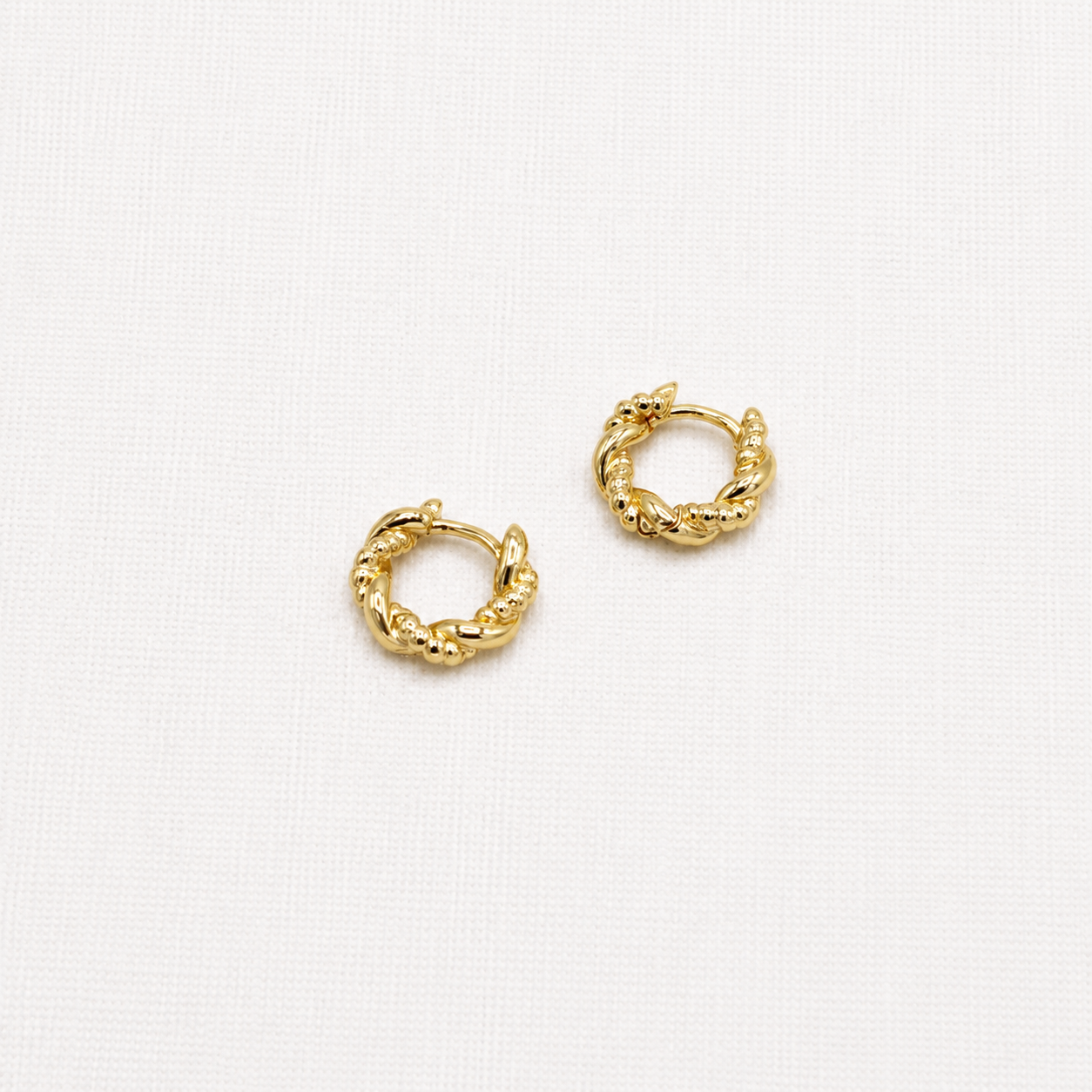 A pair of small gold huggie hoop earrings with a textured, twisted rope-like design,