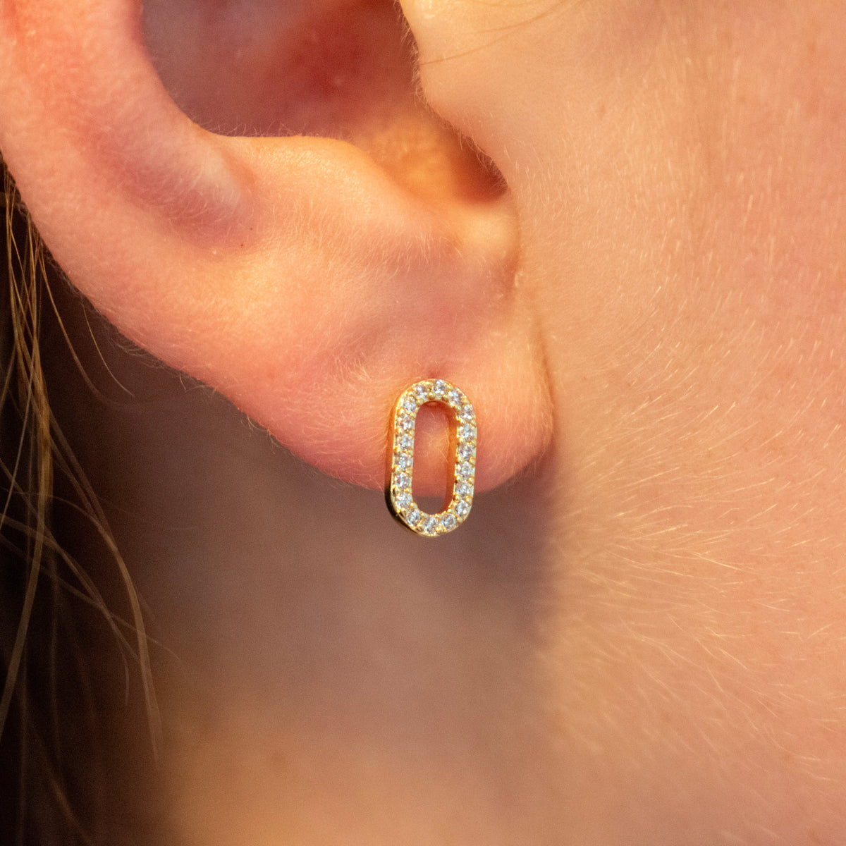 a small oval stud earring set with clear stones in a yellow gold-tone setting.