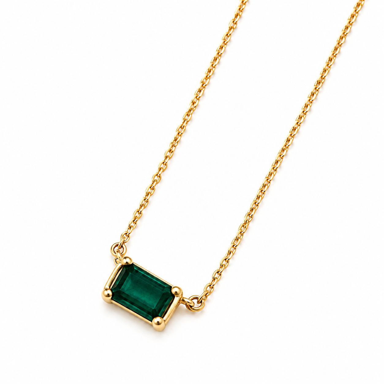 A gold chain necklace with a rectangular emerald-cut green gemstone pendant