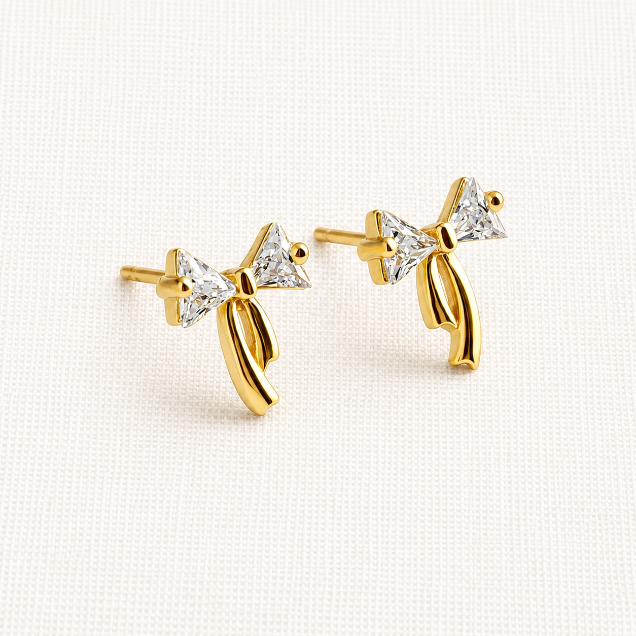 A pair of gold bow stud earrings with clear triangular gemstones