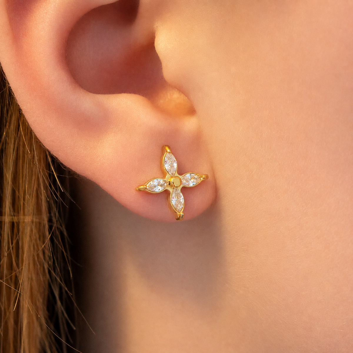 small gold stud earring with four clear marquise-cut stones arranged in a flower shape.