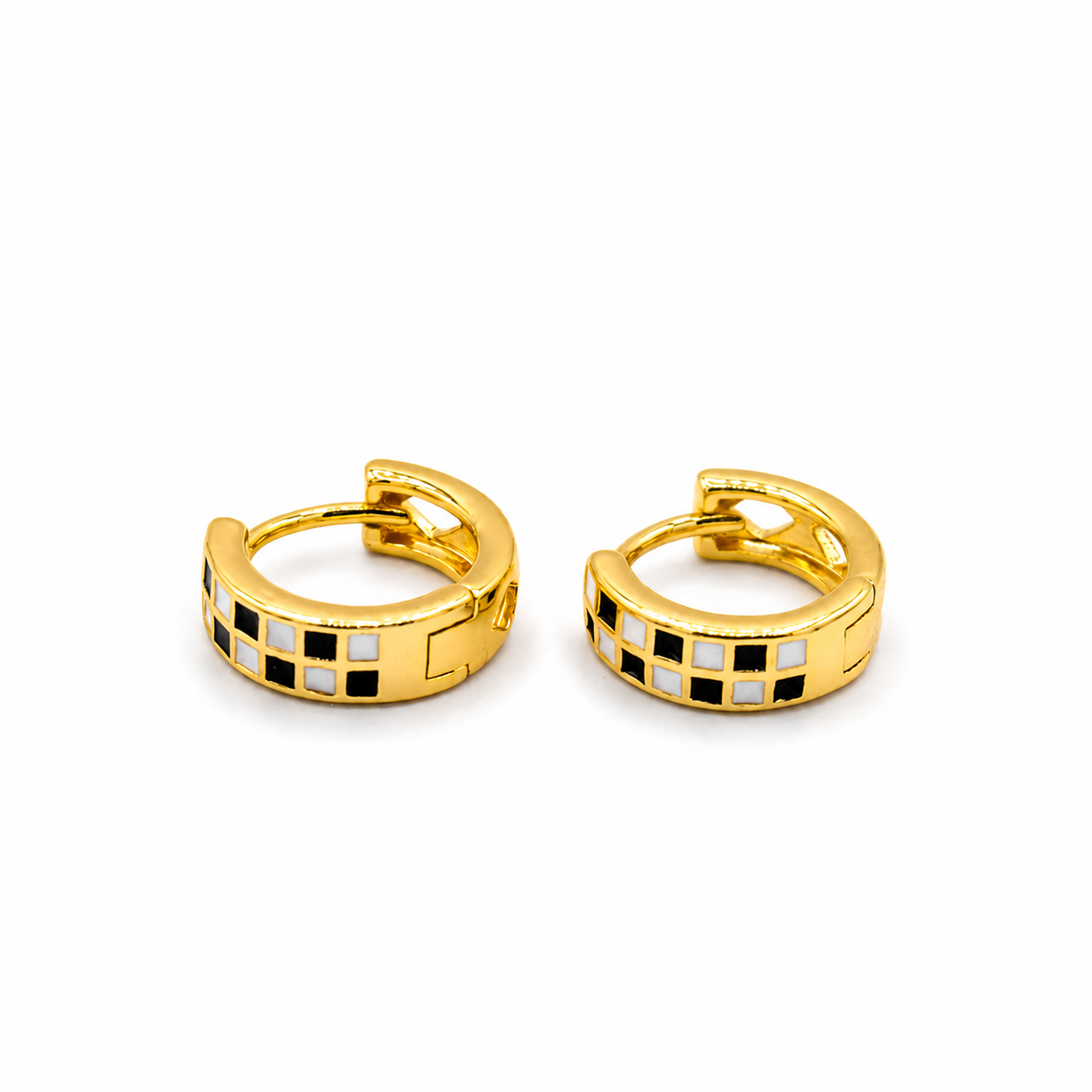 A pair of gold huggie hoop earrings with a checkered black and white enamel pattern on the front