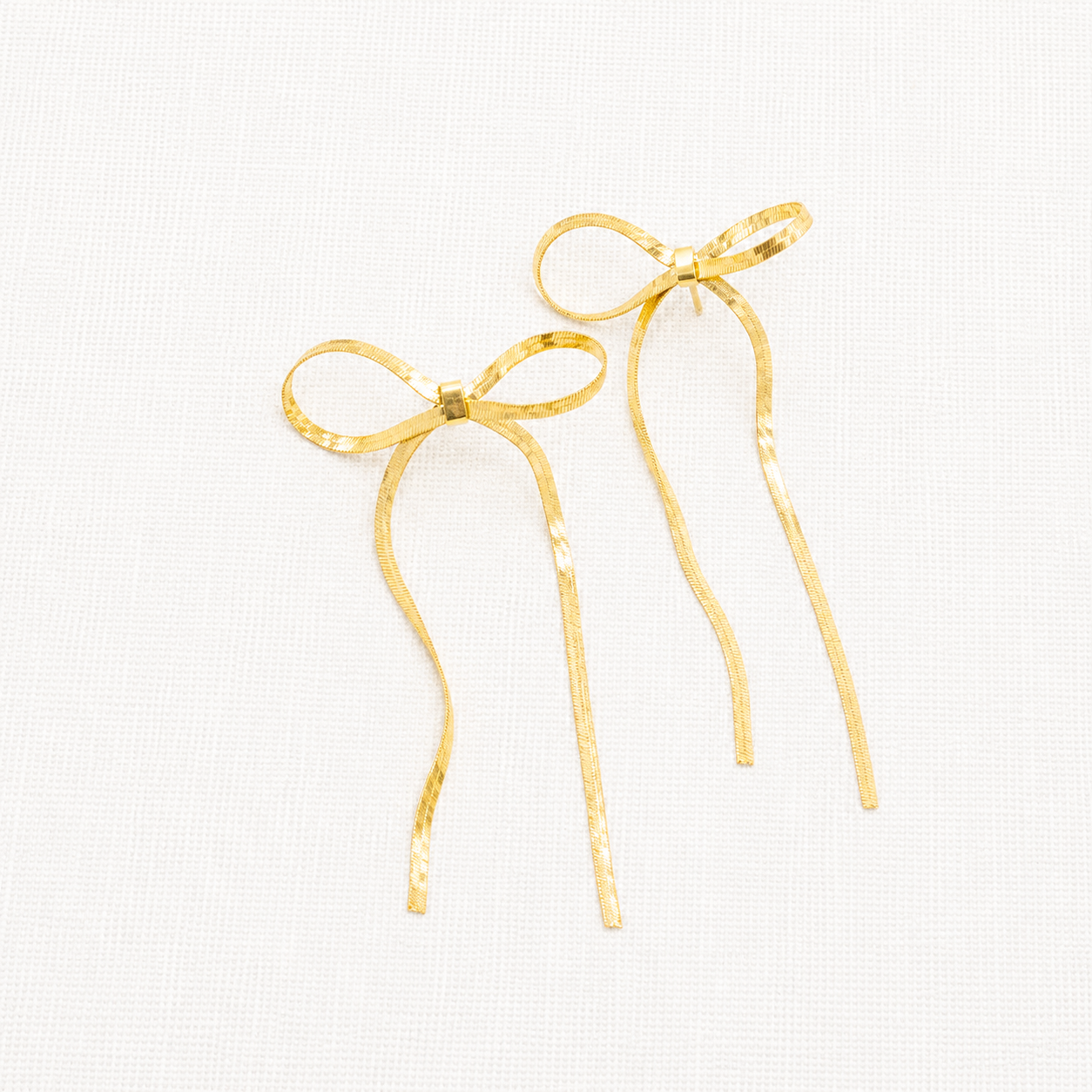 A pair of gold bow-shaped dangle earrings with long, thin ribbon-like drops