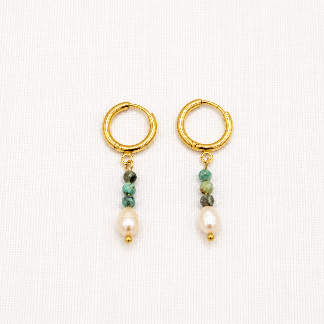 A pair of gold hoop dangle earrings with small green and gray beads and a white pearl
