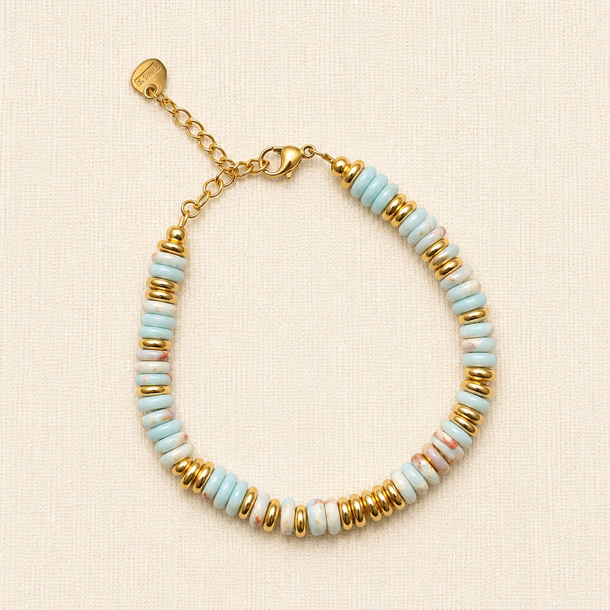 A delicate beaded bracelet with light blue and white marbled beads separated by shiny gold spacer beads, featuring a gold clasp and extender chain