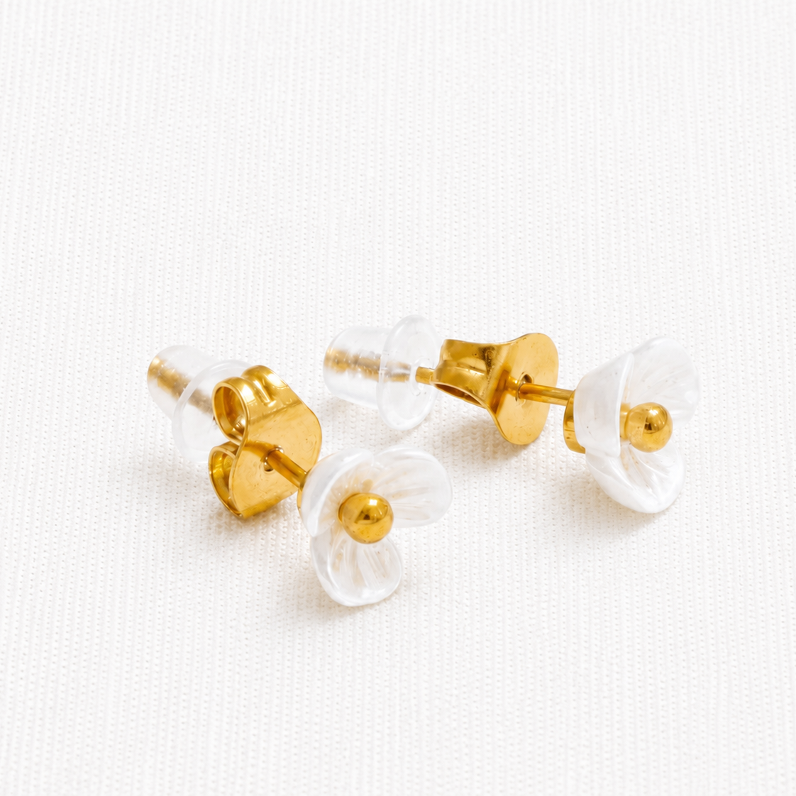 A pair of gold stud earrings with translucent white flower-shaped fronts and gold centers