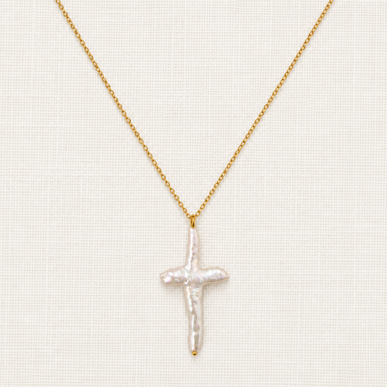 A delicate gold chain necklace featuring a textured, pearlescent white cross pendant