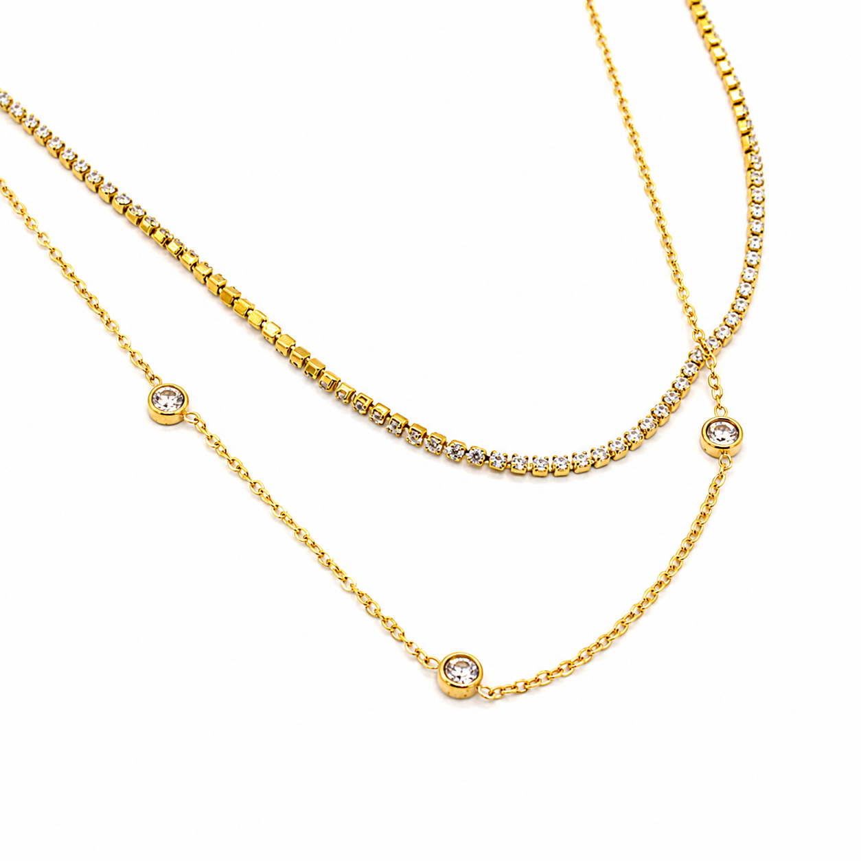 A gold-toned layered necklace set featuring a short box-link chain, a longer tennis-style chain set with small clear stones, and a delicate chain with three round bezel-set clear stones