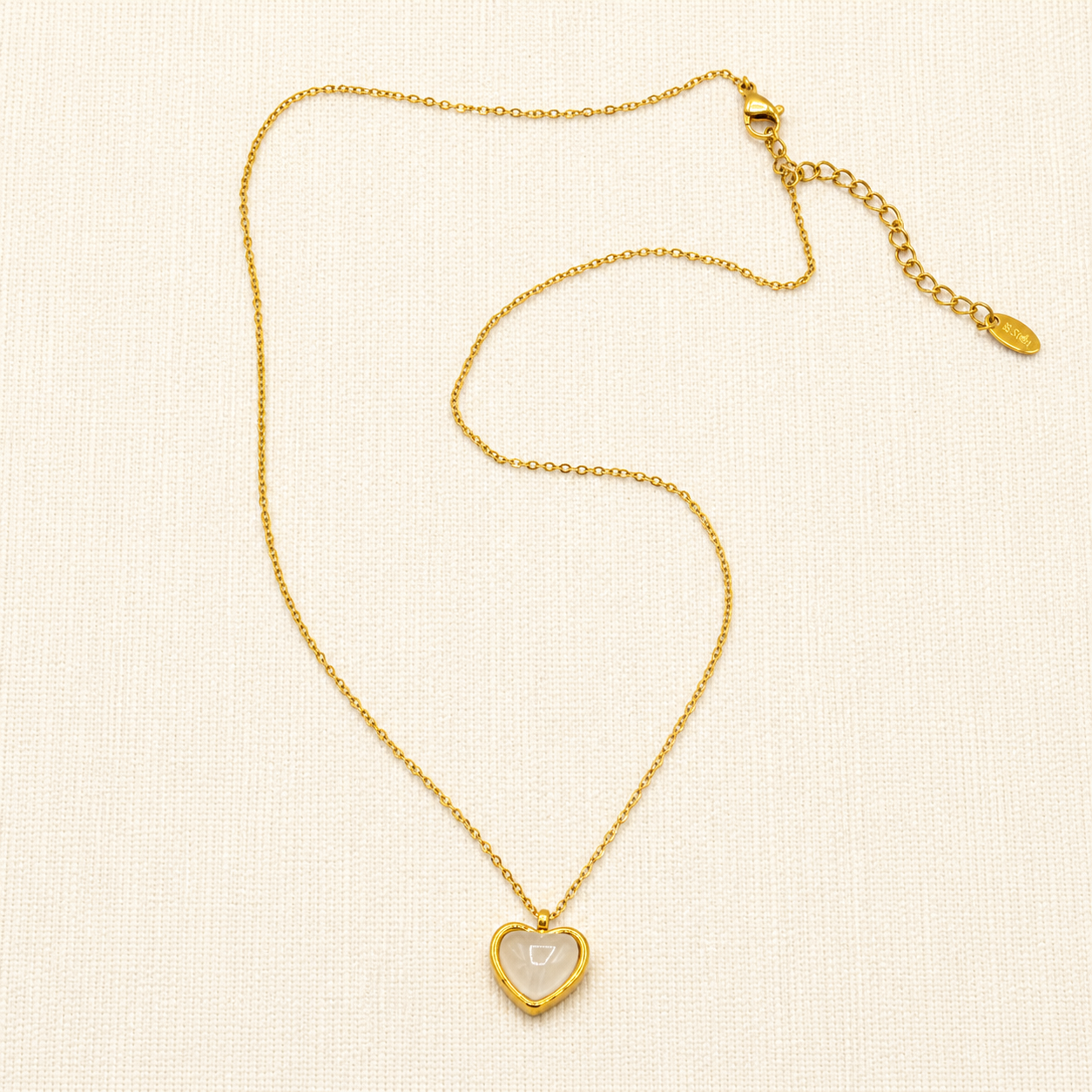A delicate gold chain necklace with a small heart-shaped pendant featuring a white inlay
