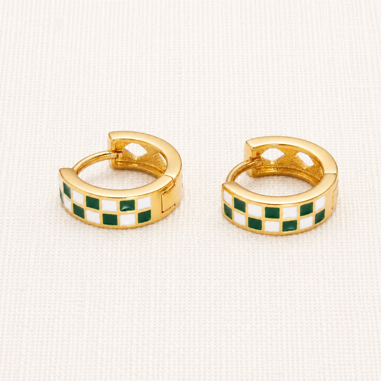 A pair of gold huggie hoop earrings with a checkered green and white enamel pattern