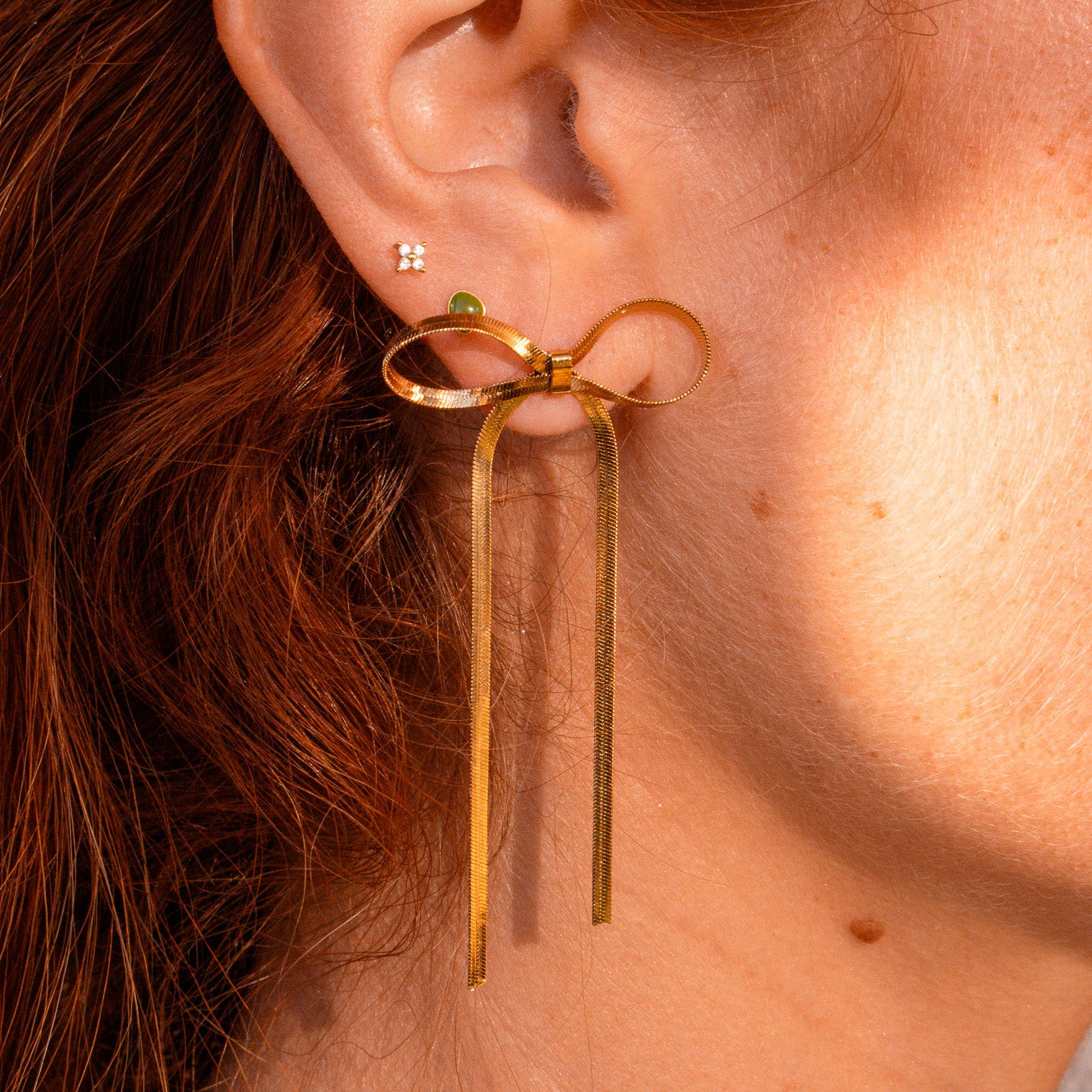 Gold bow-shaped earrings worn by a person with red hair.