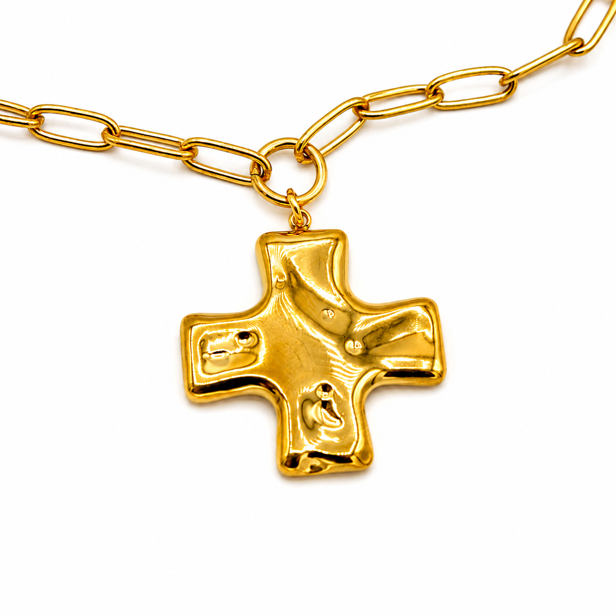 A gold cross pendant necklace with a textured, polished finish, hanging from a gold paperclip chain
